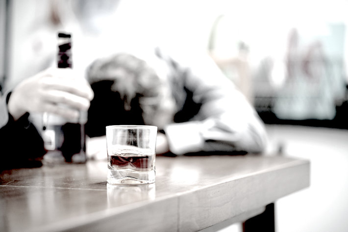 Alcoholic man on a background, focus on a glass of alcohol.